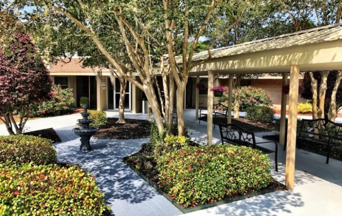A tranquil courtyard garden with trees, bushes, benches, and a small fountain.