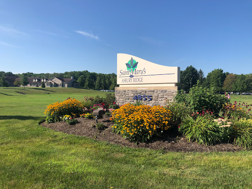 A welcoming sign surrounded by vibrant flowers and greenery, set against a clear blue sky.