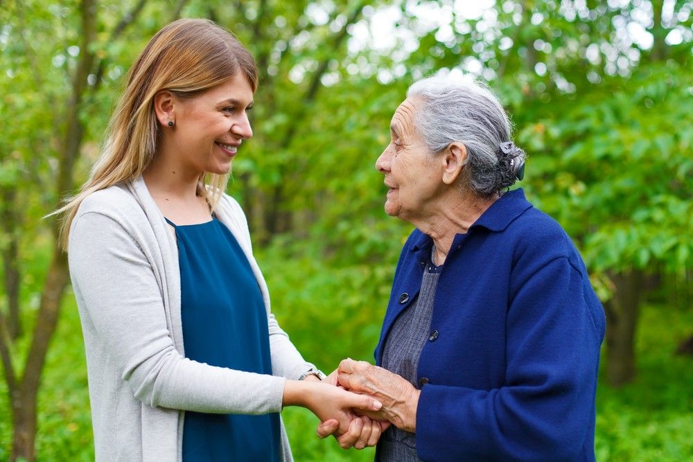 A younger woman and an elderly woman smiling and holding hands in a park.