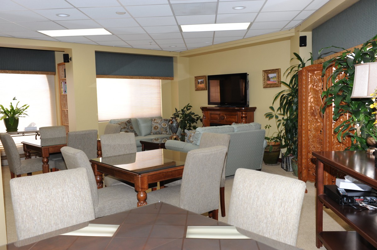 A cozy living room with a television, sofas, chairs, and indoor plants.