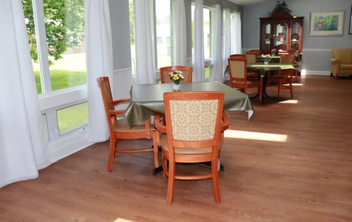 A cozy dining room with wooden chairs and tables set near large windows with flowing curtains.