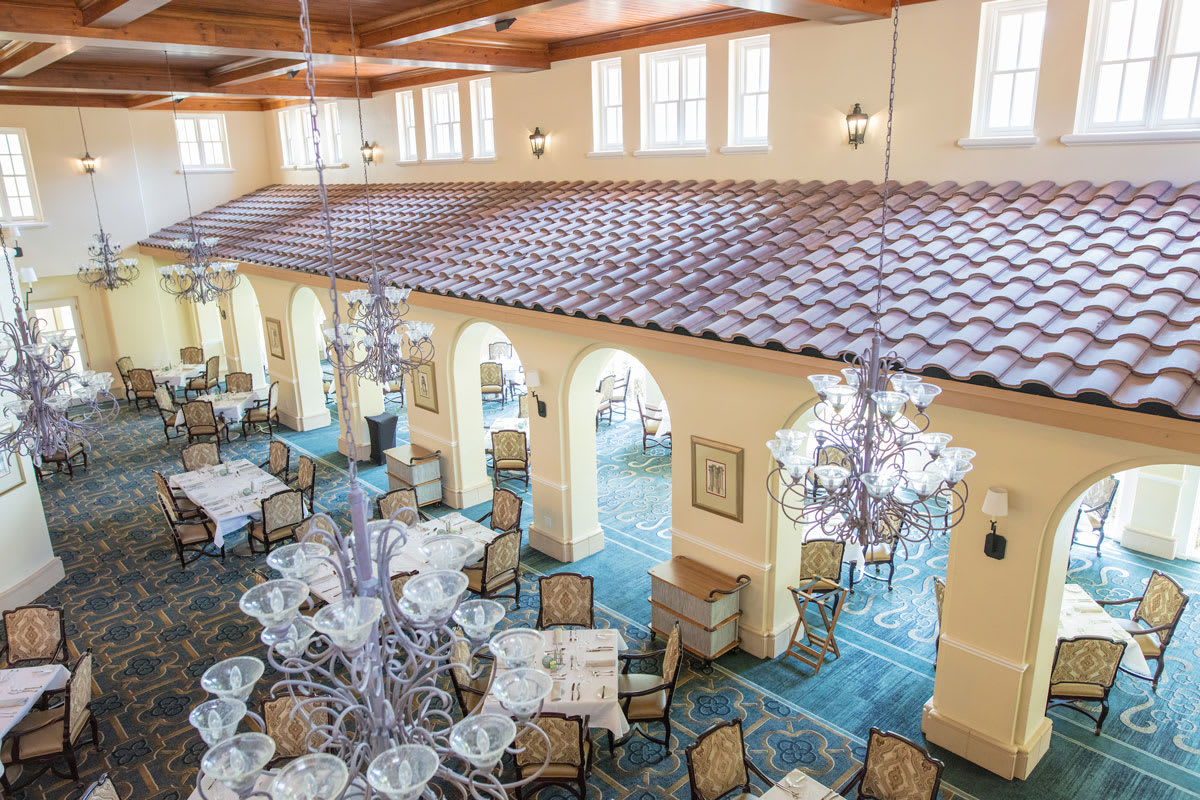 A luxurious dining room with elegant chandeliers, beautifully set tables, and arched windows.