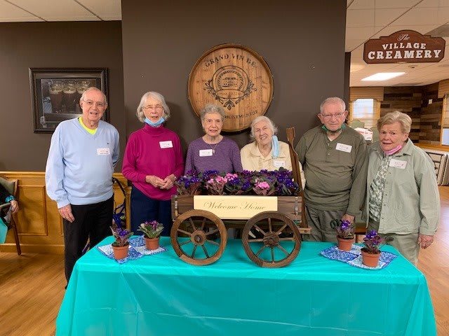 A group of seniors smiling and standing behind a decorated table at an event.