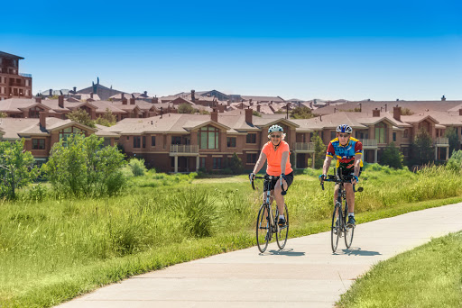 Two cyclists enjoying a sunny day on a pathway surrounded by greenery and residential homes.