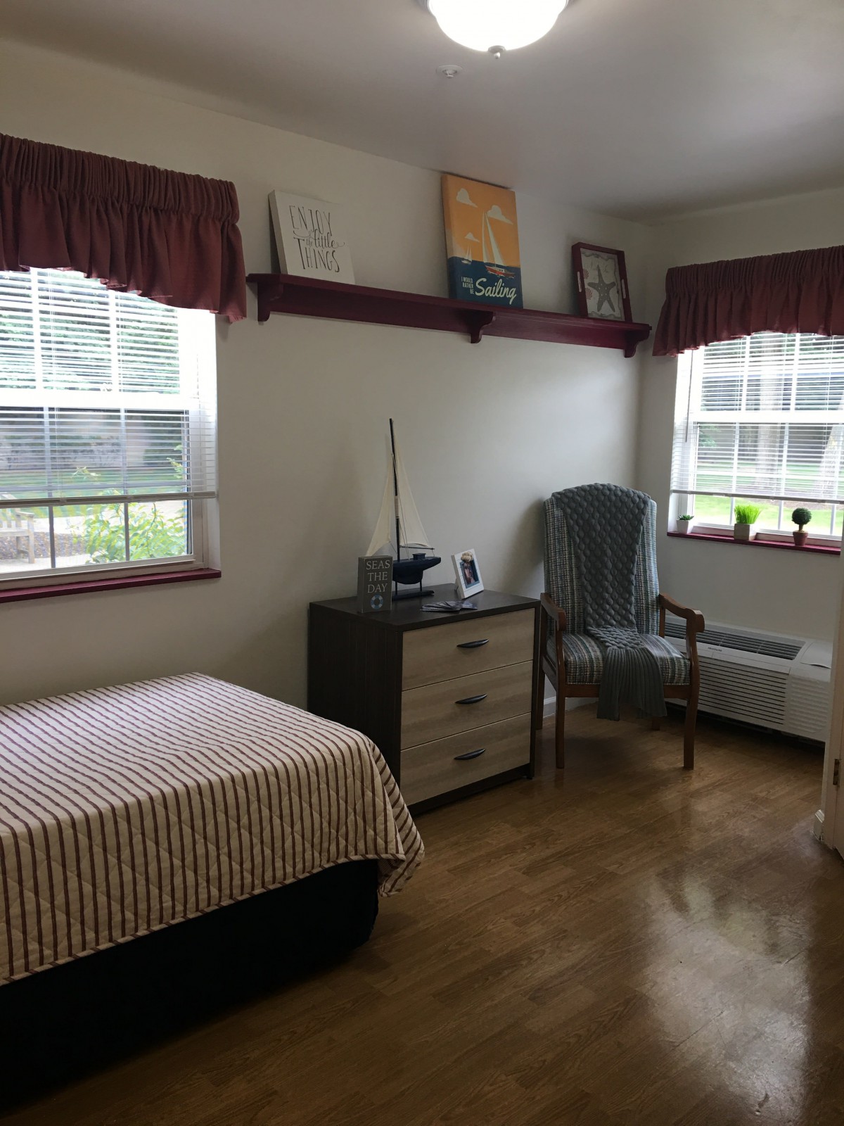 A cozy bedroom with a single bed, a chair, and two windows allowing natural light.