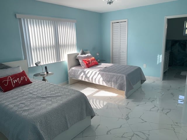 A bright bedroom with twin beds and minimalist decor, featuring blue walls and a marble floor.