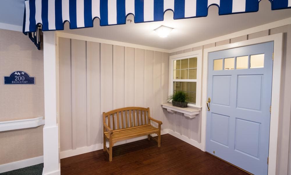 A cozy porch featuring a wooden bench and a blue door, with a striped awning overhead.