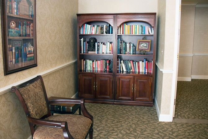 A cozy corner featuring a wooden bookshelf filled with books and an upholstered chair.