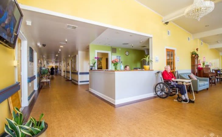 A bright and welcoming reception area in a nursing home, featuring a hallway and a person in a wheelchair.