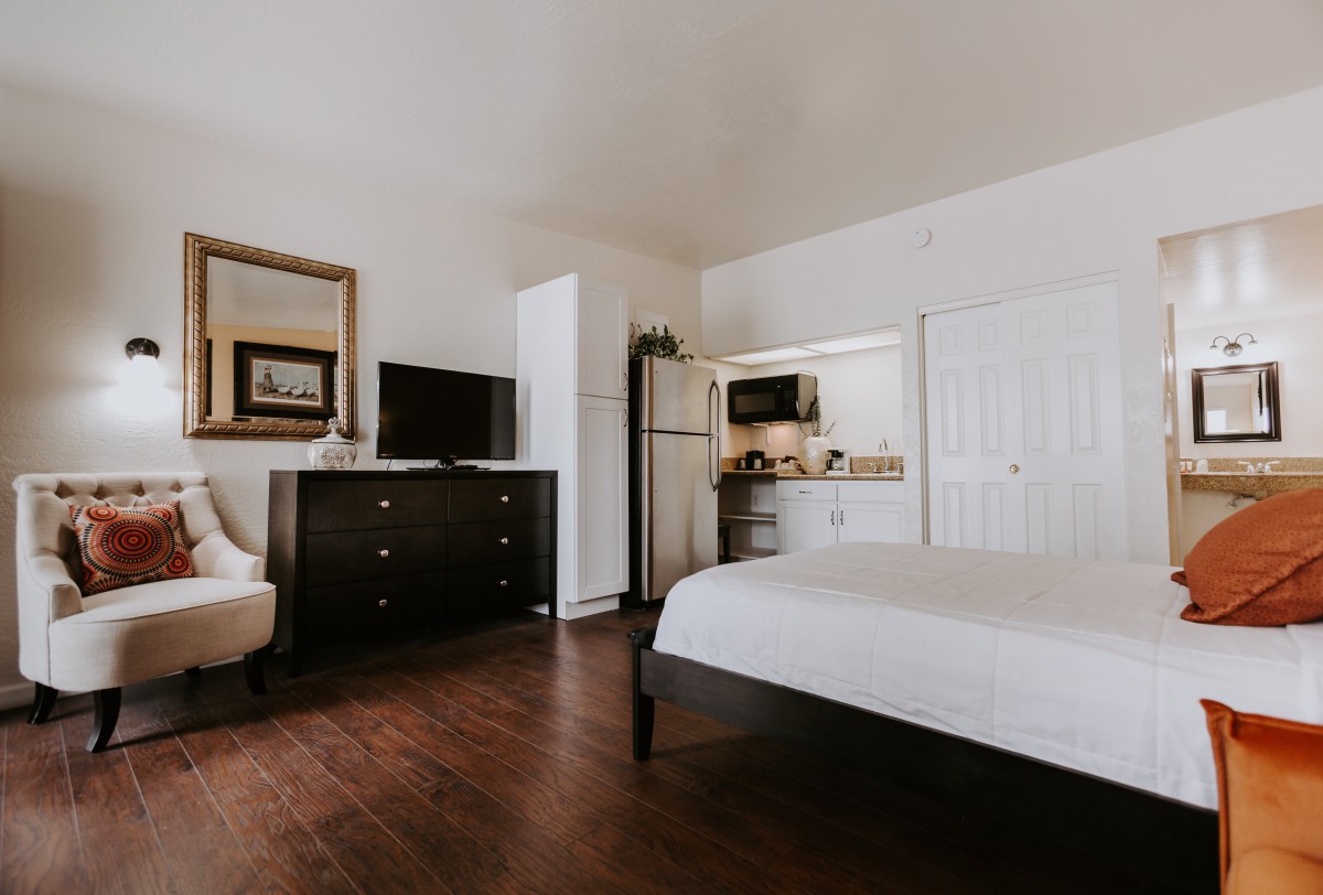 A minimalist bedroom with a kitchenette, featuring a bed, dresser, and television.
