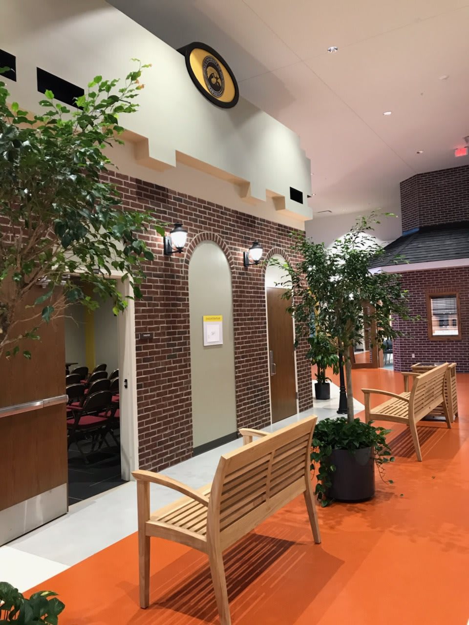 A hallway with wooden benches, potted plants, and a clock above a brick facade.