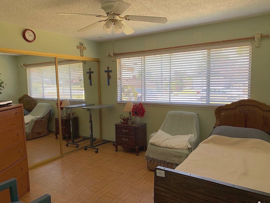 A cozy bedroom with a bed, mirror closet, and large windows with blinds.