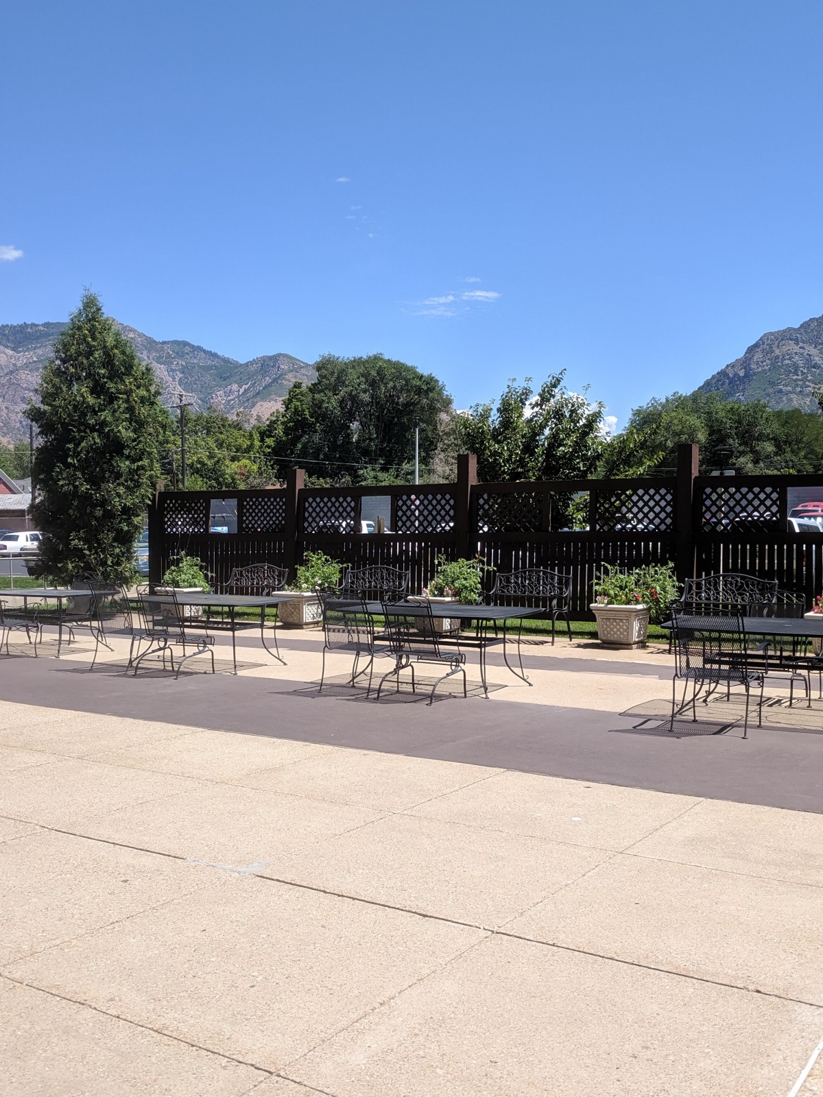 Outdoor seating area with tables and chairs, set against a backdrop of mountains under a clear blue sky.