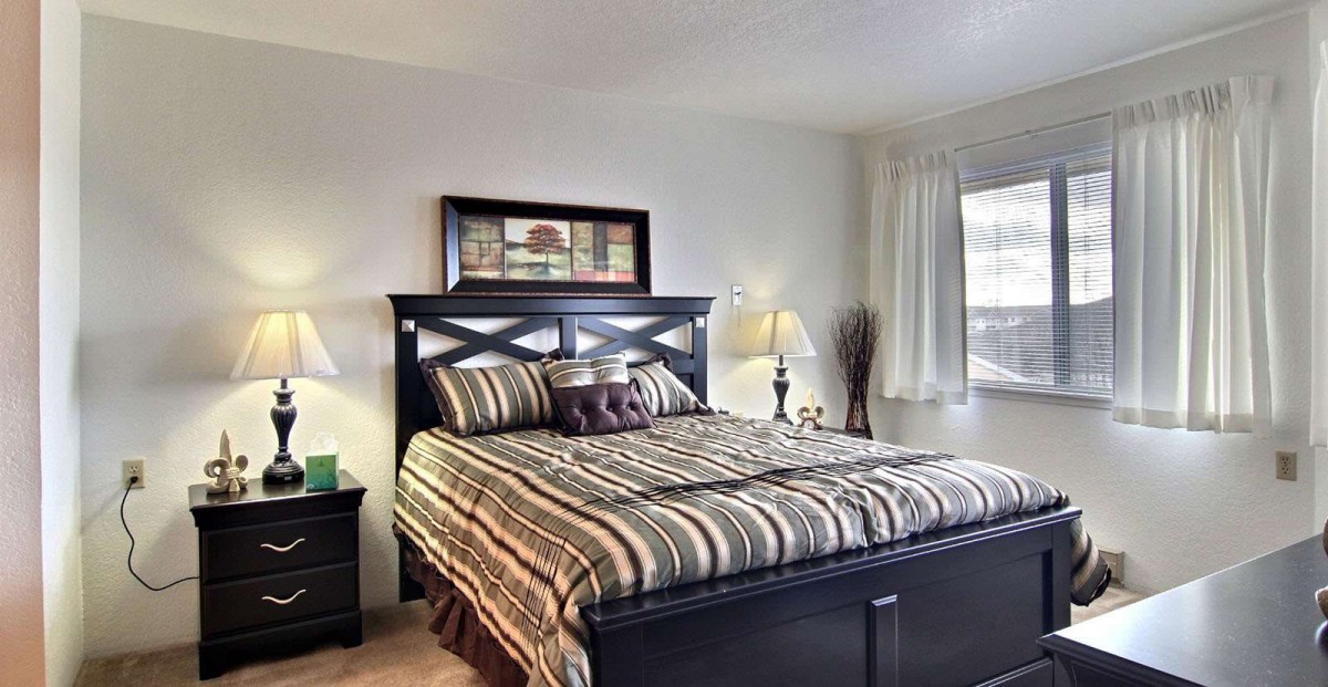 A cozy bedroom with a neatly made bed, bedside lamps, and a large window allowing natural light.