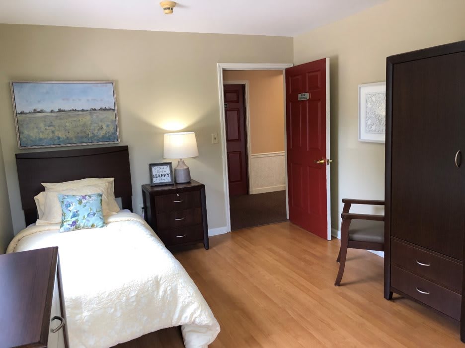 A cozy bedroom with a single bed, lamp, and wooden floor.
