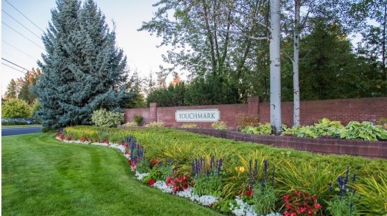 A beautifully landscaped garden with colorful flowers and lush greenery, framed by a brick wall and trees.