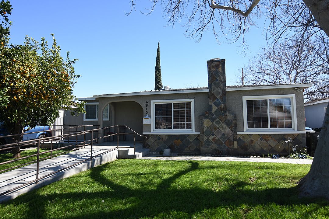 A single-story house with a stone chimney and well-maintained lawn under a clear blue sky.