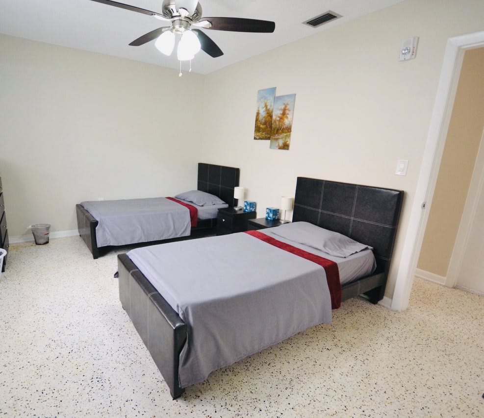 A modern bedroom with two beds, featuring gray bedding and a ceiling fan.