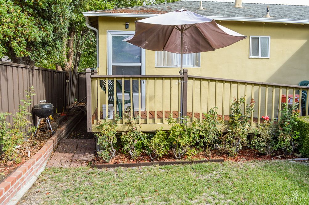 A cozy backyard with a wooden deck and patio umbrella, featuring a small garden and landscaping.