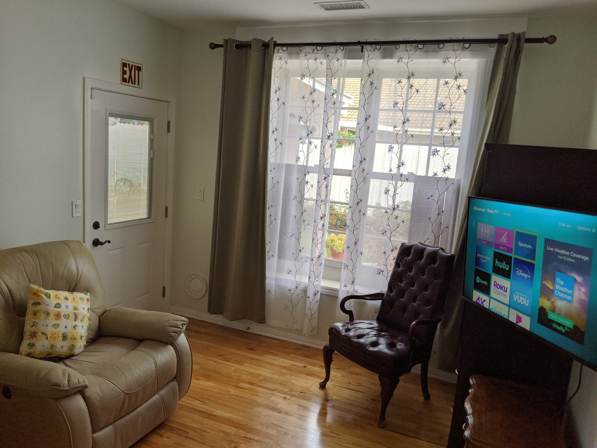 A cozy living room with an armchair, television, and large window with curtains.
