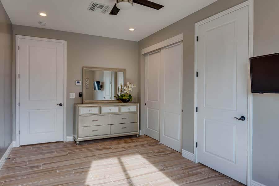 A modern bedroom interior featuring a dresser with a mirror, neutral color palette, and wooden flooring.