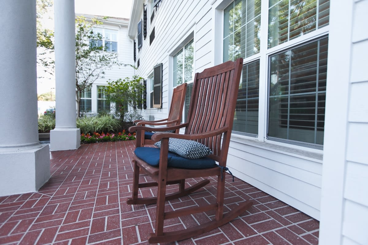 Wooden rocking chairs on a brick porch of a house.