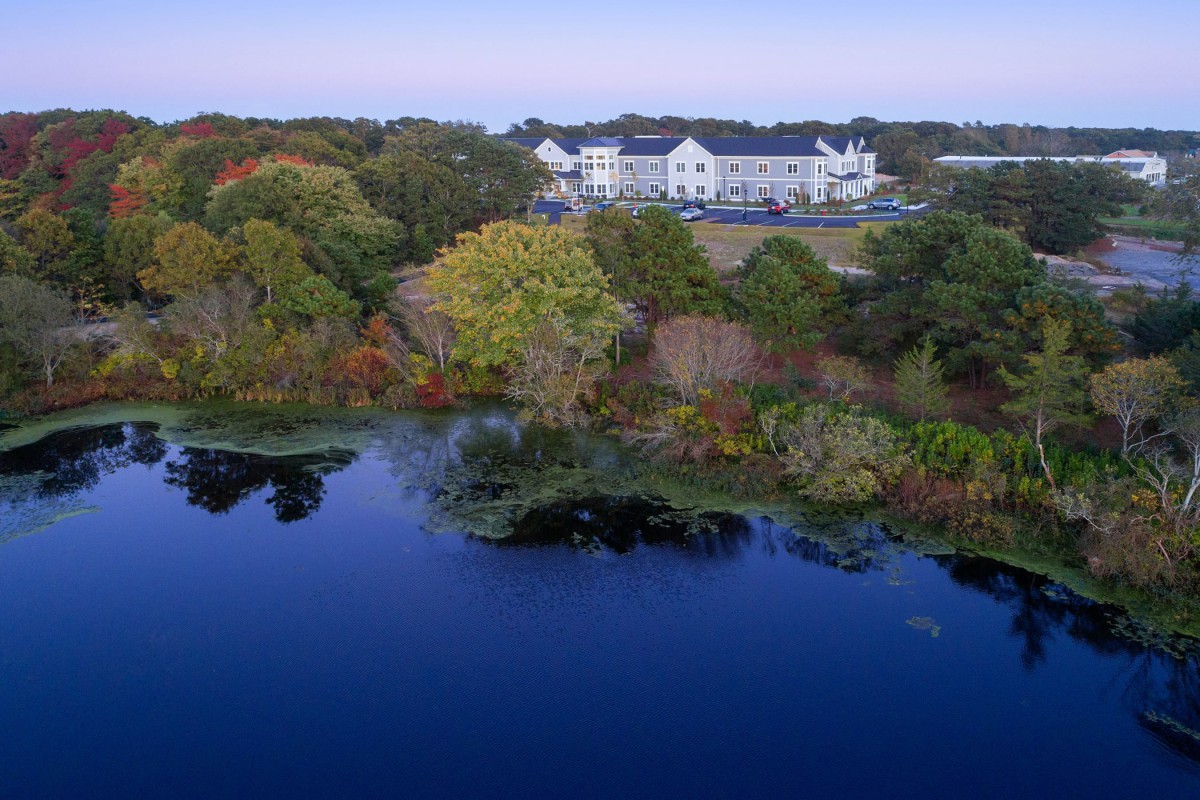 A serene view of a building surrounded by autumn trees and a calm lake reflecting the scenery.