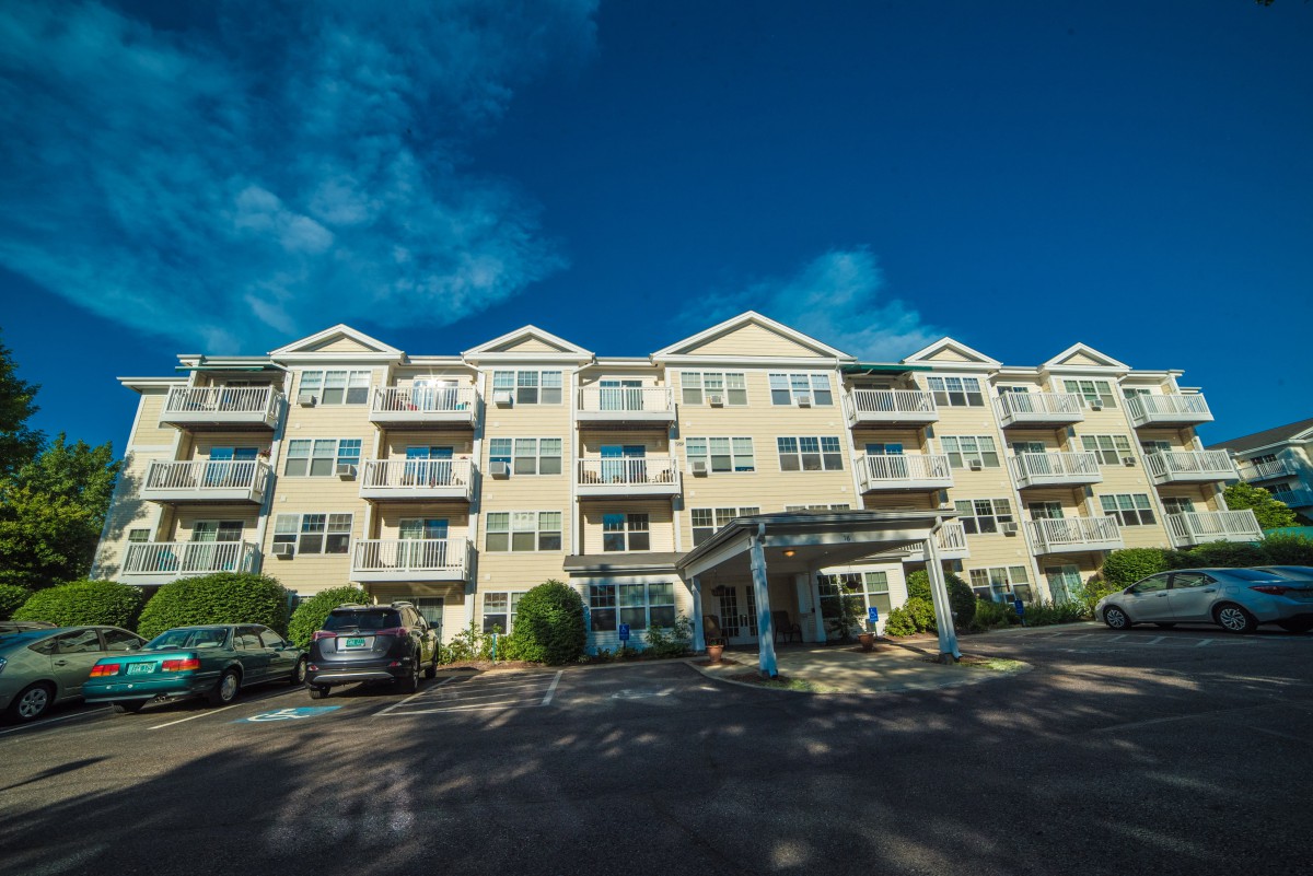 A modern apartment building with a parking lot under a partly cloudy sky.