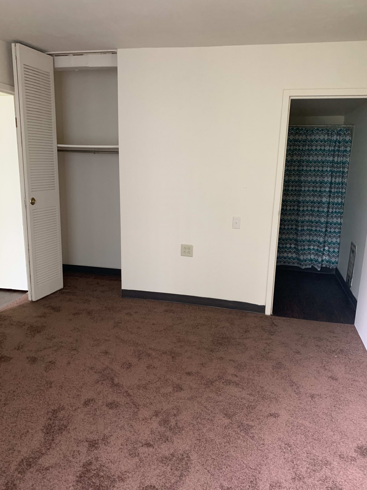 An empty room with carpet flooring, featuring a closet and an open door leading to a bathroom.