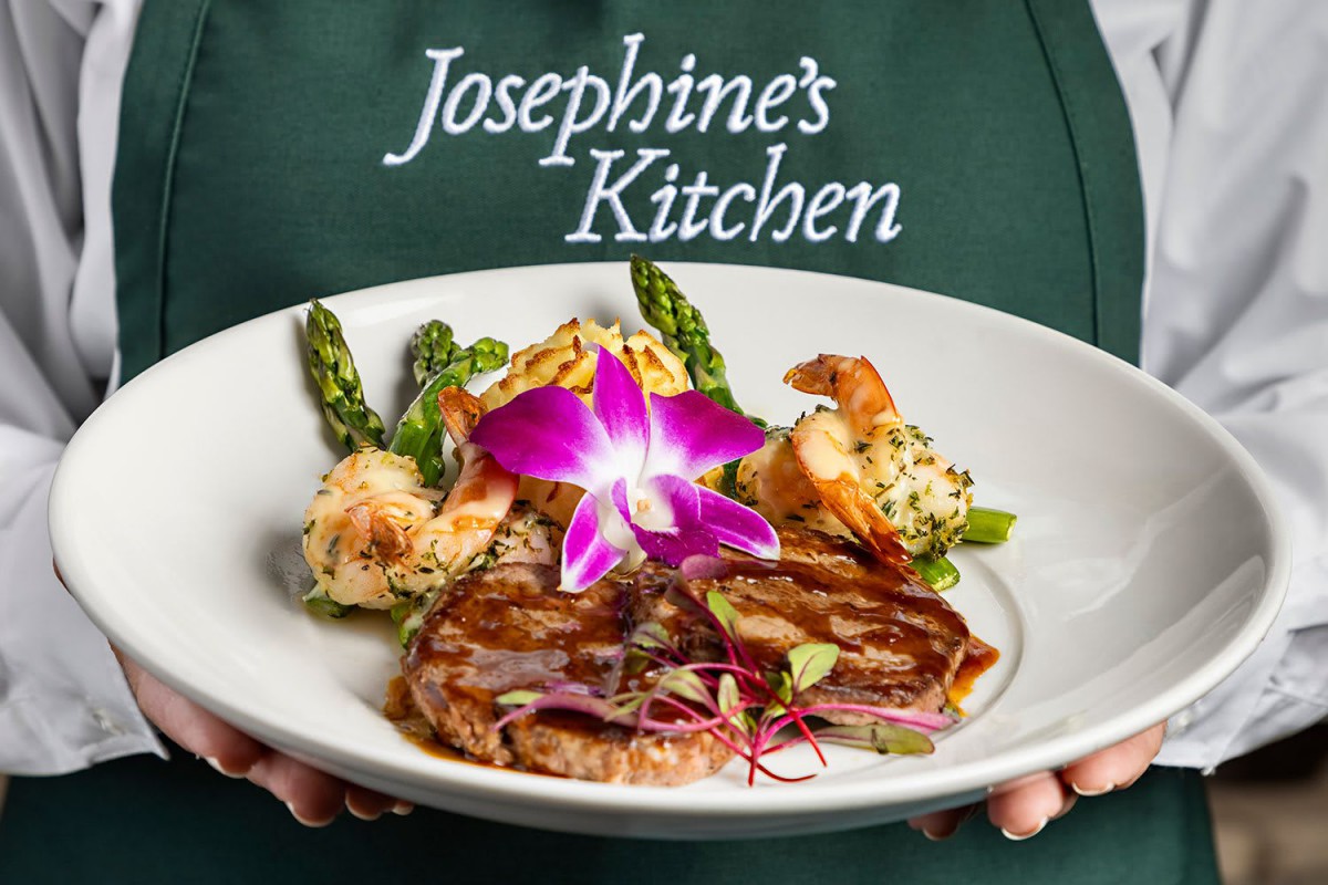 A beautifully plated gourmet dish at Josephine's Kitchen featuring shrimp and asparagus with a floral garnish.