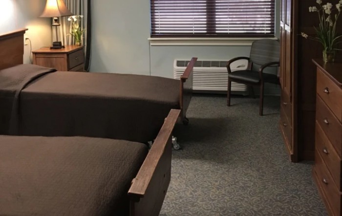 A hospital room with two beds and chairs near a window.
