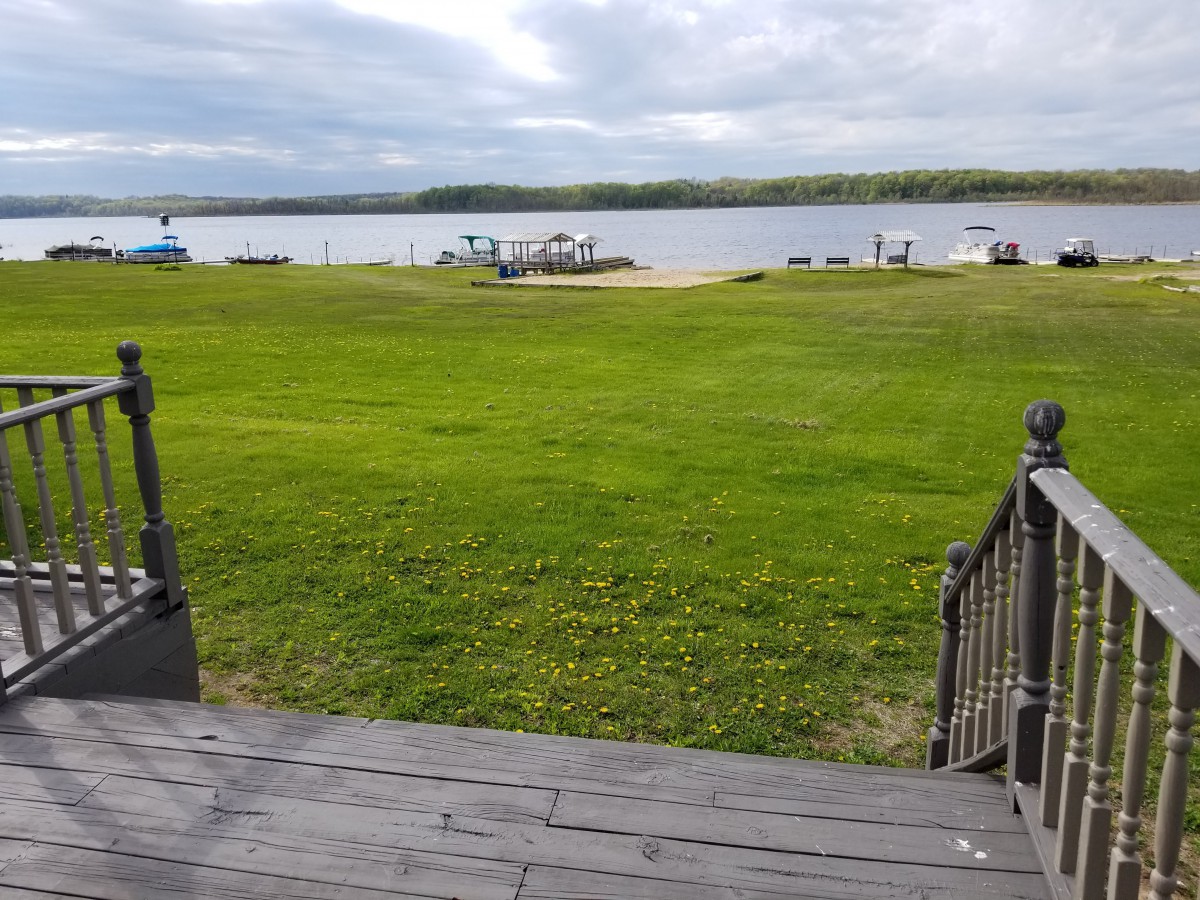A scenic view of a grassy area leading to a lake with boats and a dock under an overcast sky.
