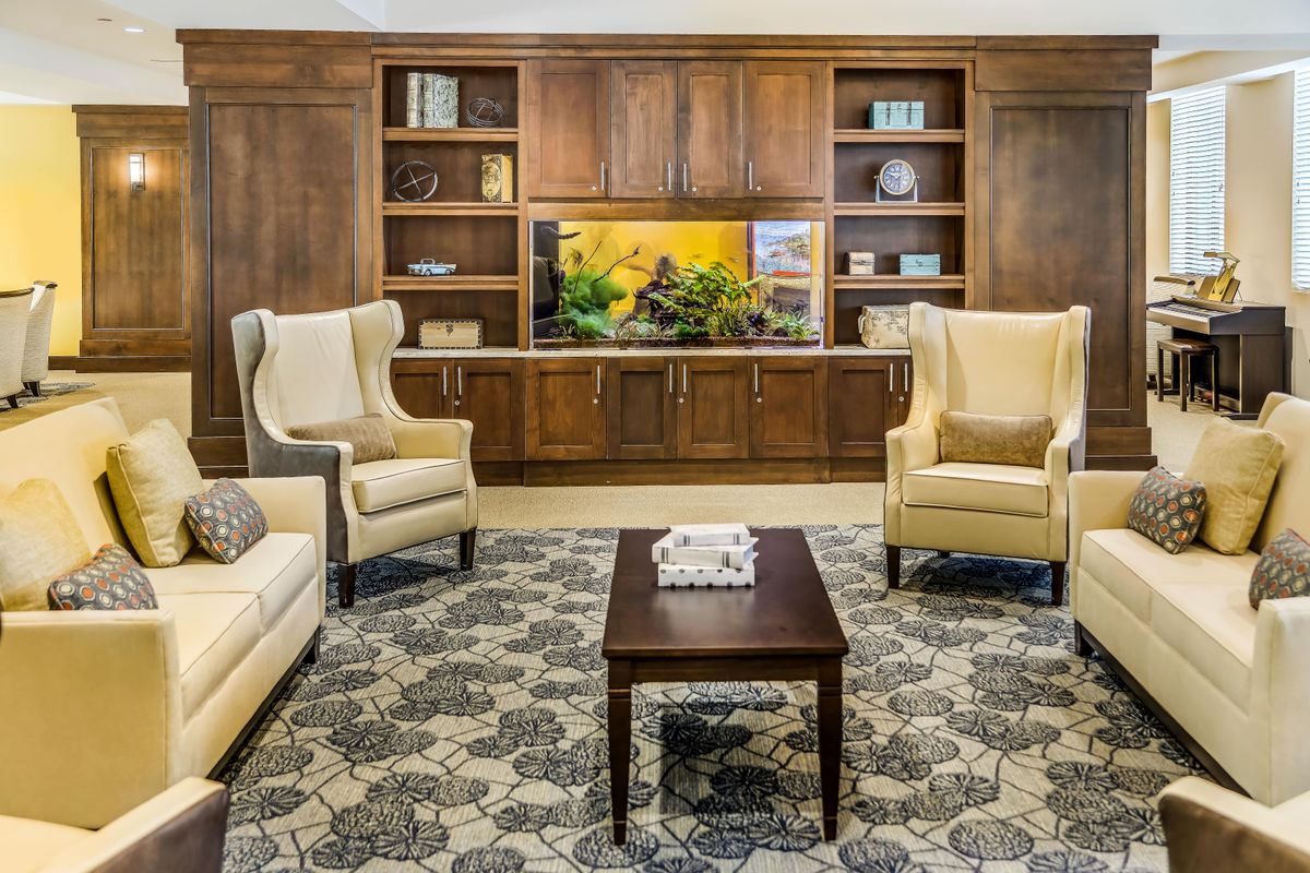 A cozy living room with elegant furniture, featuring a large aquarium set within wooden bookshelves and a decorative rug.