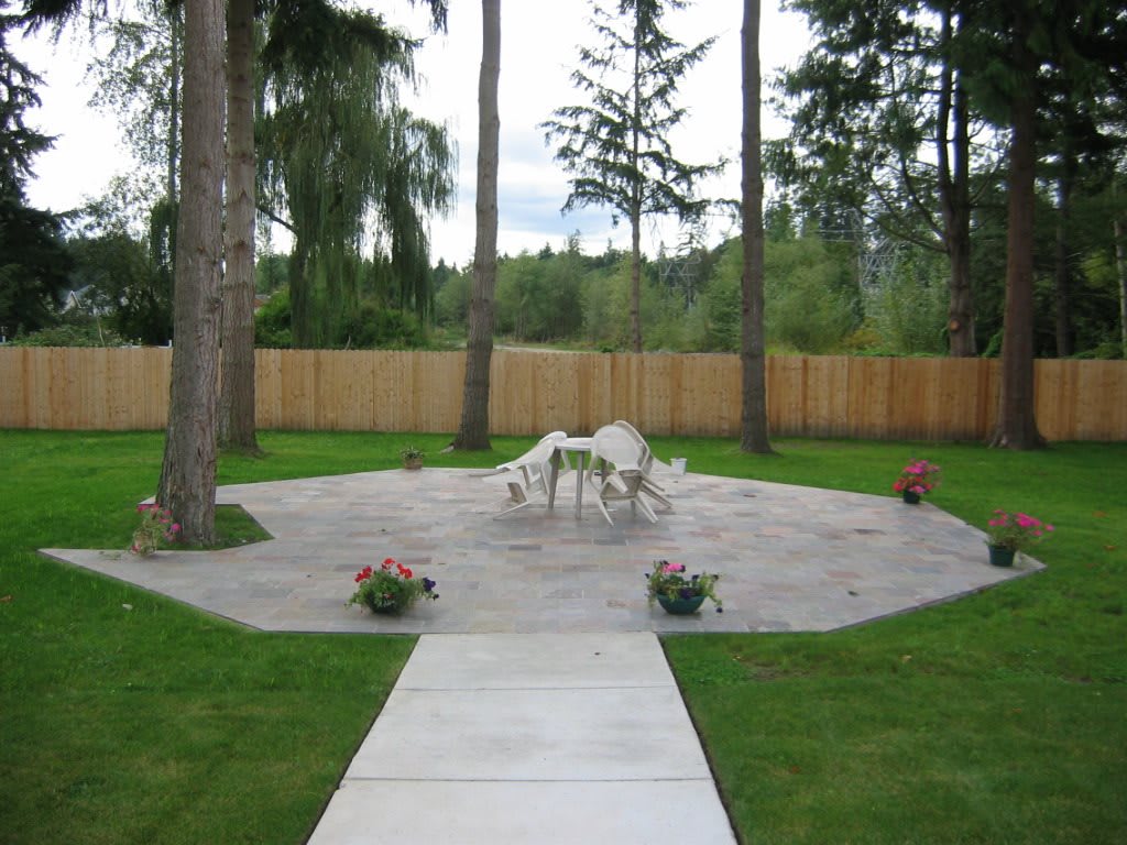 A serene backyard patio area with outdoor furniture surrounded by grass and trees.