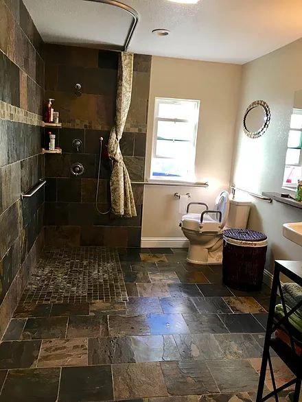 A spacious bathroom with tiled flooring, featuring a walk-in shower, toilet, sink, and mirror.