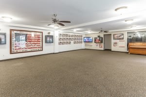 An interior room with wall art and photographs, featuring a carpeted floor, ceiling fans, and a television.