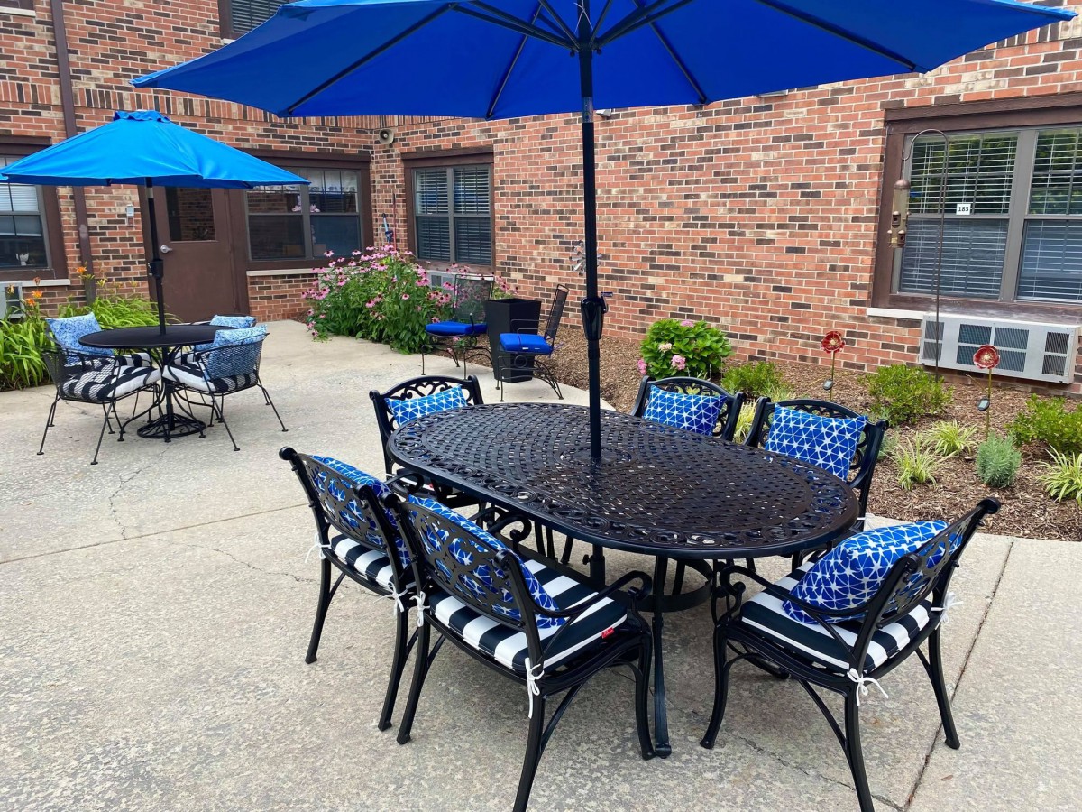 An inviting outdoor patio area with a table and chairs under blue umbrellas, next to a brick building.