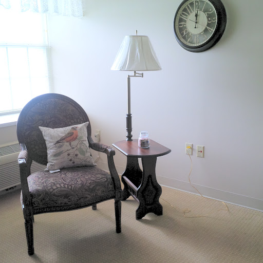 A cozy corner featuring an elegant armchair, a stylish lamp, and a small side table beside a wall clock.