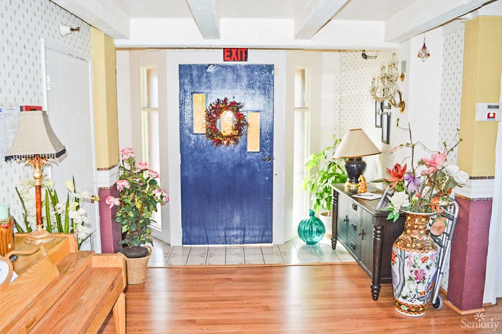 A cozy interior featuring a blue door adorned with a wreath, surrounded by plants and furniture.