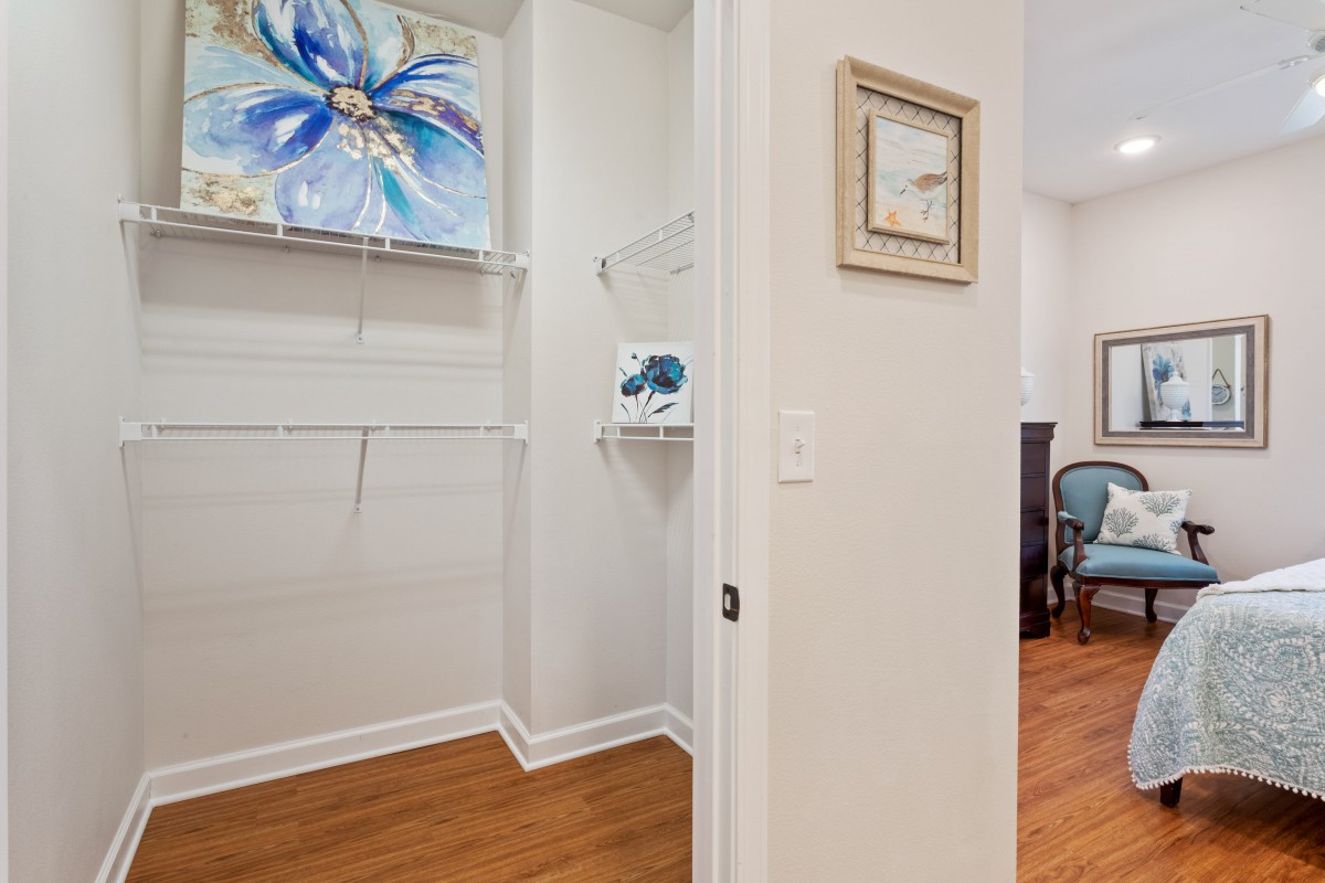 A small closet with wooden flooring, featuring artwork and shelves.