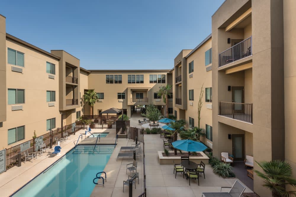 A modern apartment complex with a swimming pool and outdoor seating area featuring umbrellas.