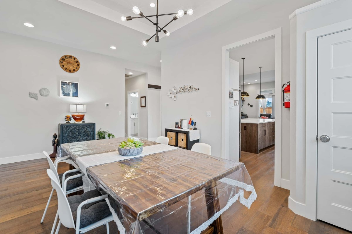 A modern dining room with a wooden table, contemporary lighting, and an open view into the kitchen.