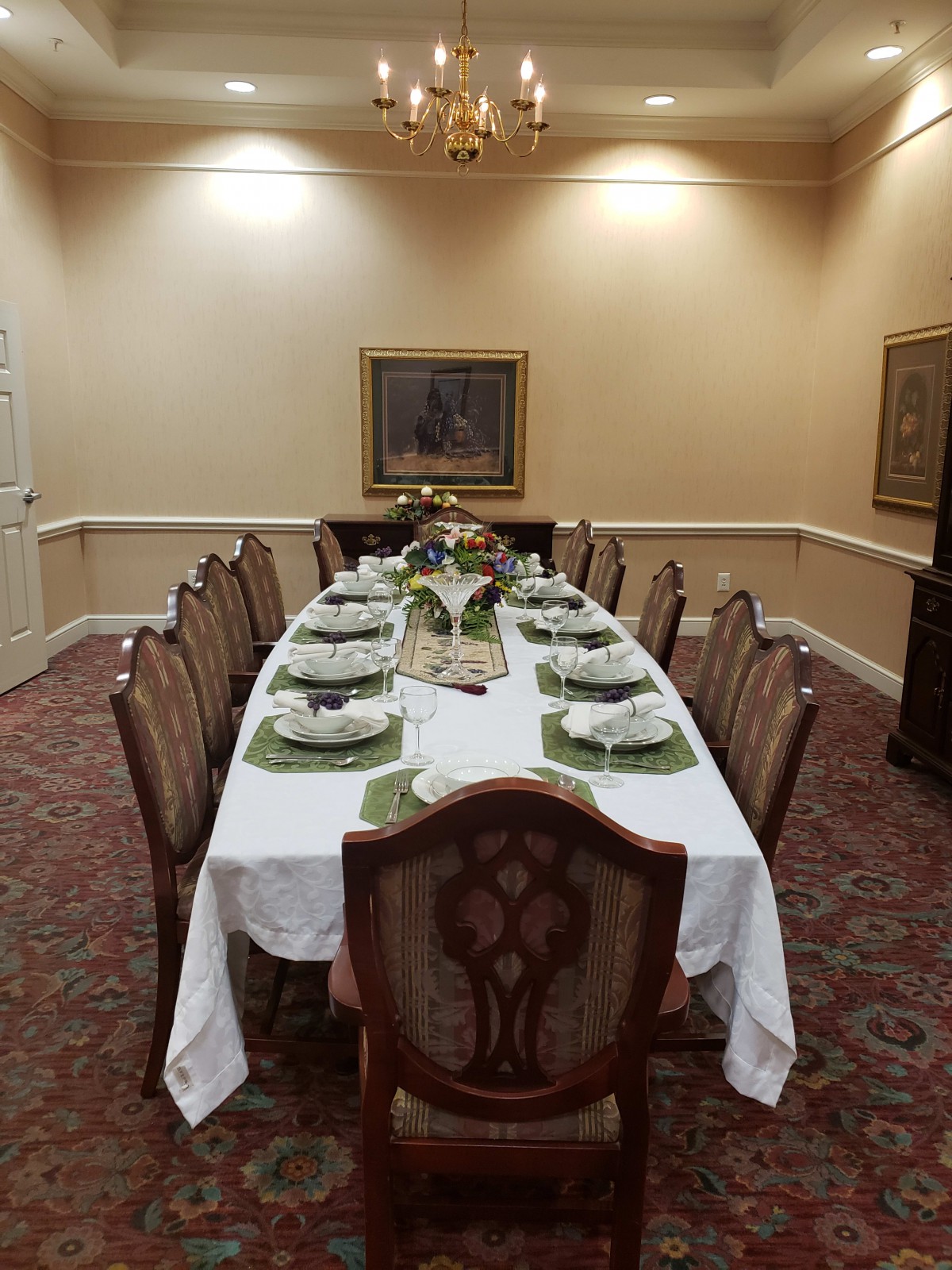 A formally set dining table with elegant chairs and white tablecloth in a warmly lit room.