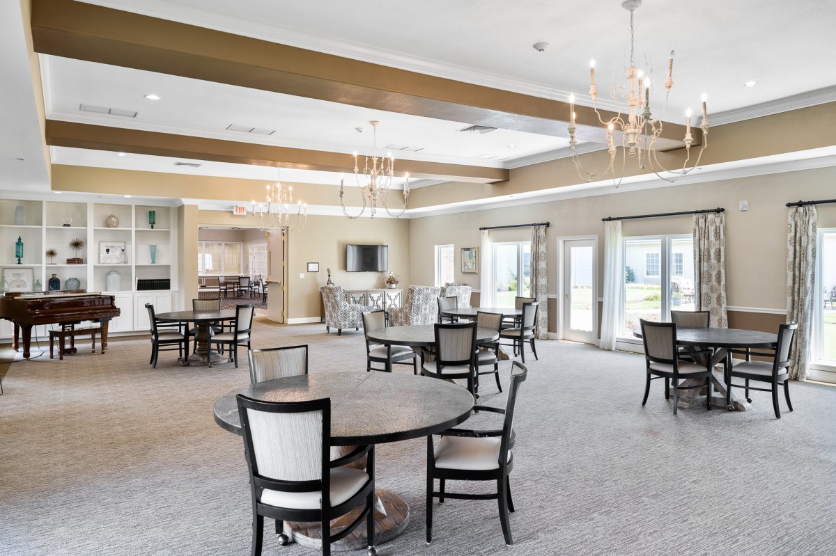 A spacious and elegantly designed dining area featuring round tables, chairs, and chandeliers.