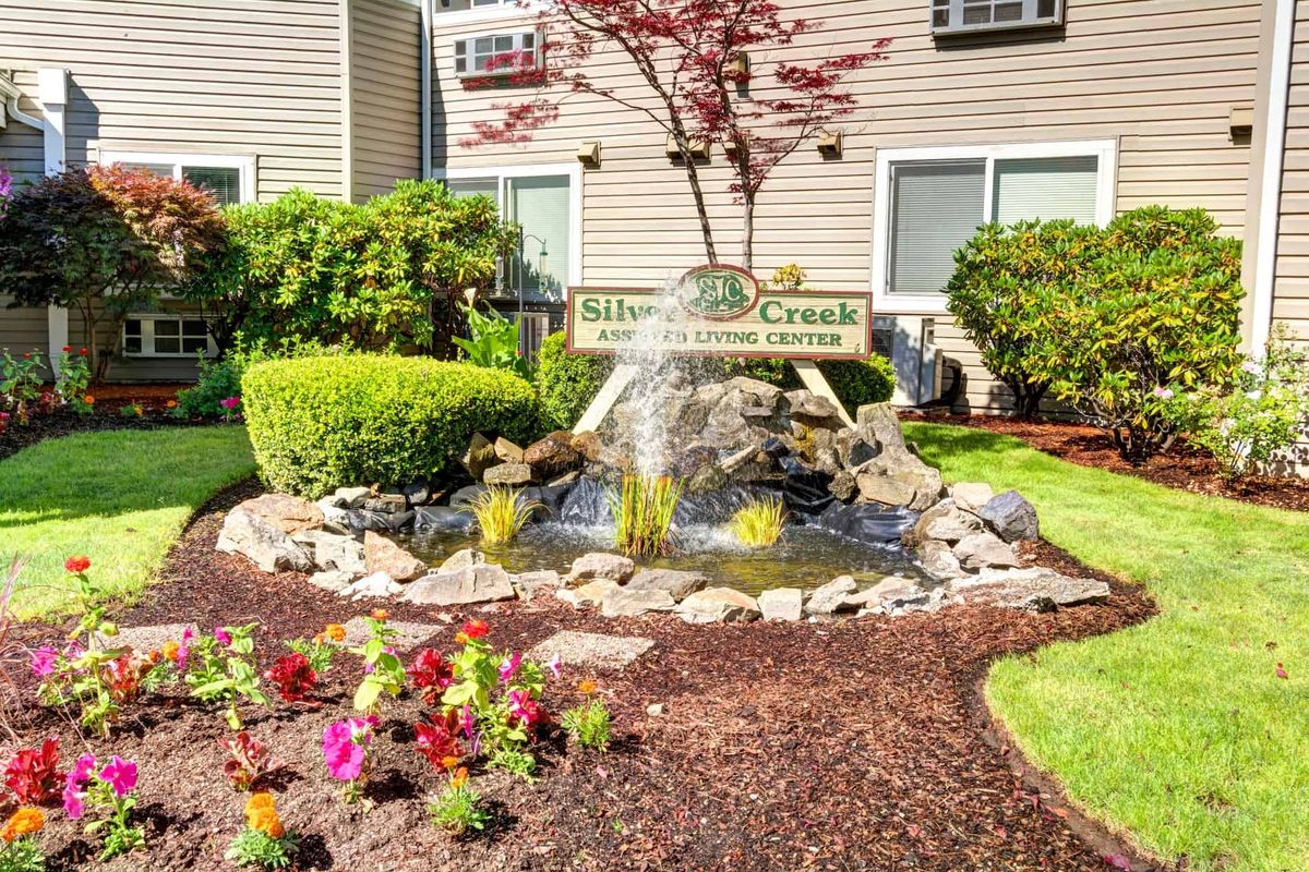 A beautifully landscaped garden with a small fountain and colorful flowers in front of a building.
