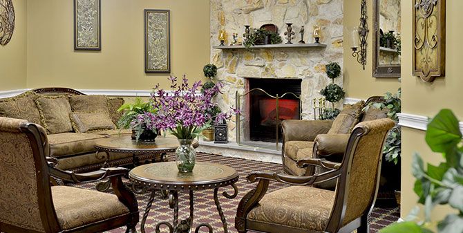 A cozy living room with a stone fireplace, elegant armchairs, and a coffee table adorned with flowers.