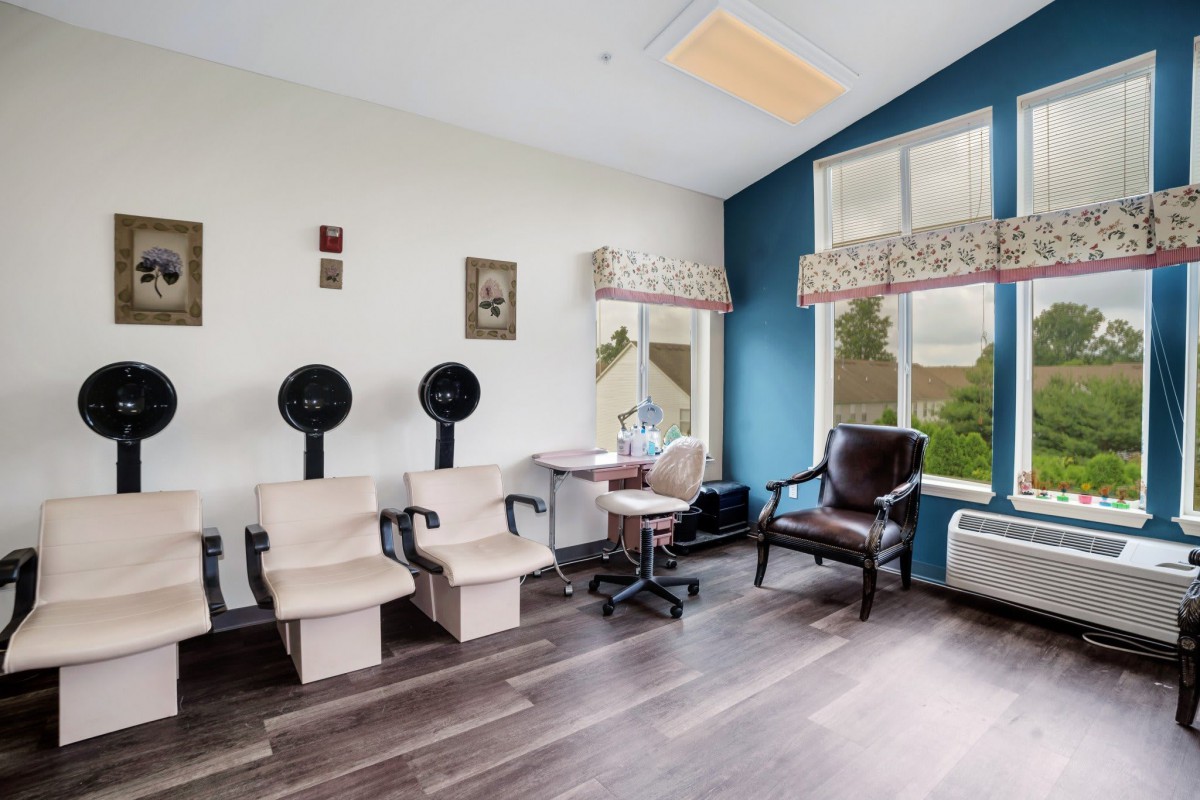 A cozy beauty salon interior featuring hair dryers, comfortable chairs, and a large window allowing natural light.