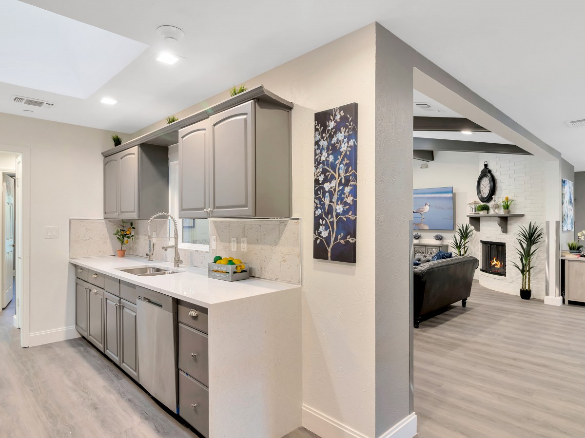 A modern kitchen with gray cabinets opens into a spacious living room, showcasing an open floor plan.