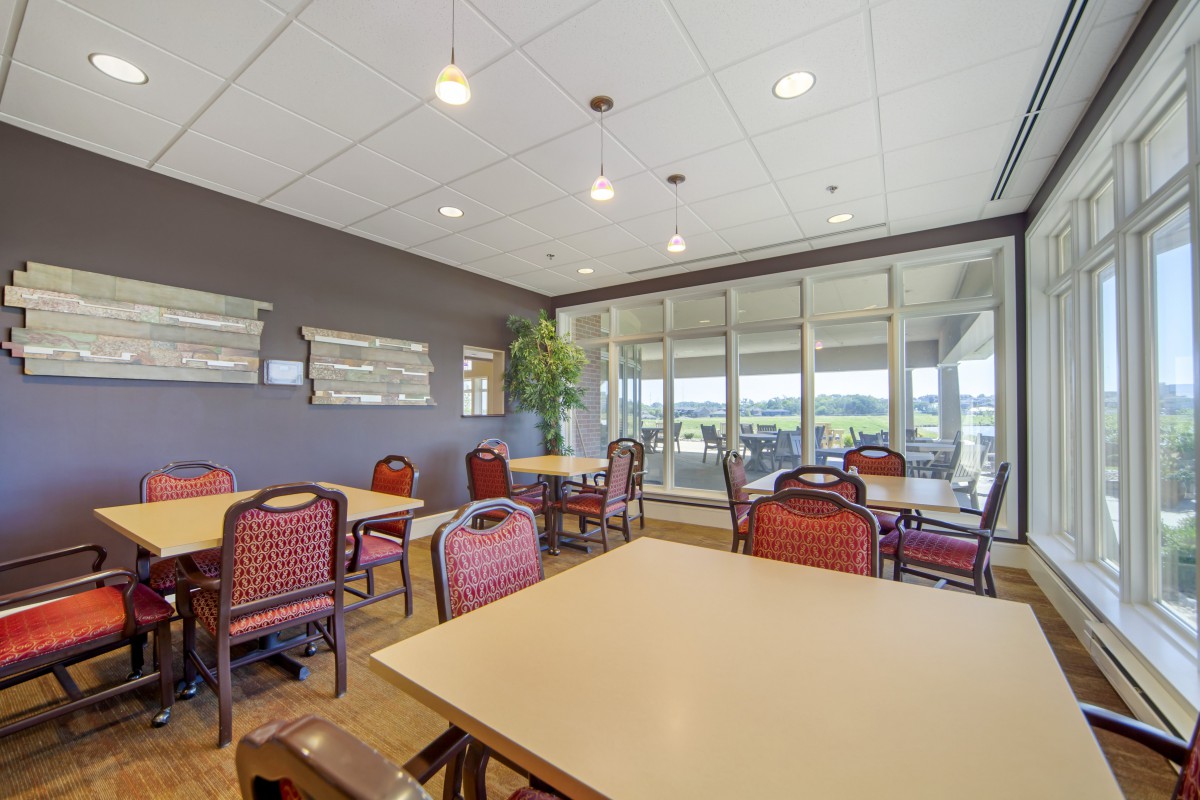An empty dining area with tables and chairs, featuring large windows.