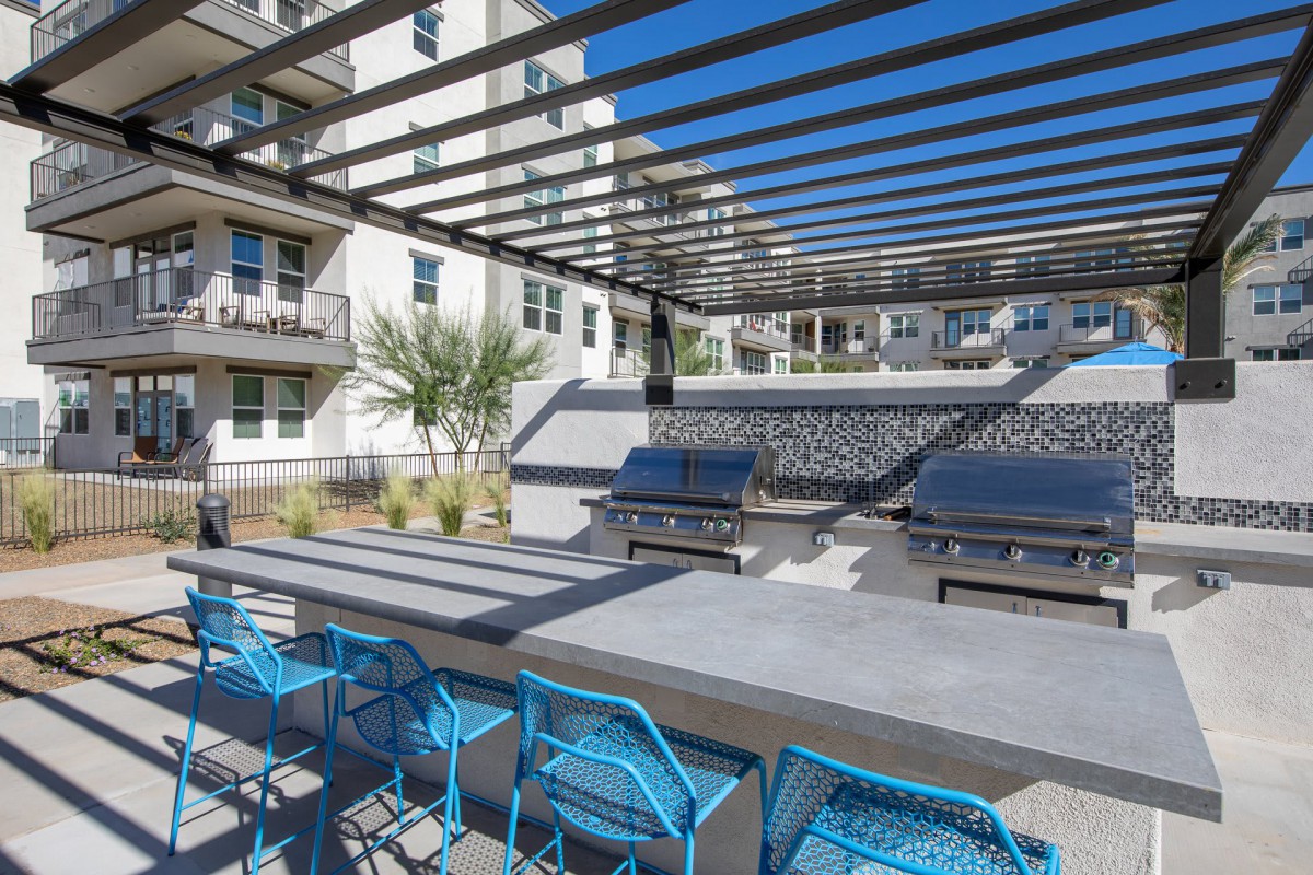 A modern outdoor patio with blue chairs and a pergola in an apartment complex.